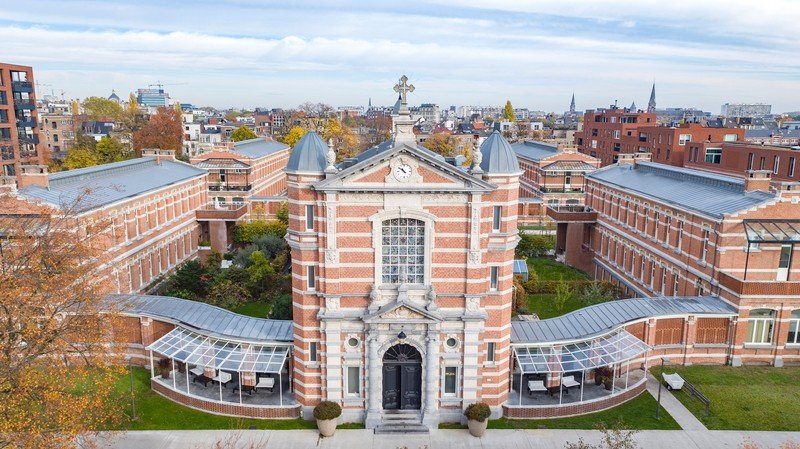 Luchtfoto van het Groen Kwartier in Antwerpen: het oude militair hospitaal met zijn
                rood-witte bakstenen gevel, de klokkentoren en de glazen serres, met de stad erachter.